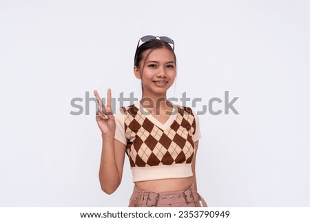 A young Filipino woman makes a peace sign. wearing a patterned shirt,shorts and white sneakers. Whole body shot isolated on a white background.