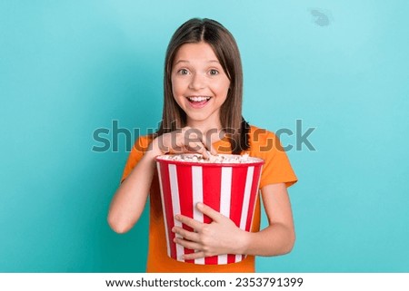 Portrait of satisfied schoolgirl with straight hair dressed orange clothes eat popcorn watch movie isolated on turquoise color background