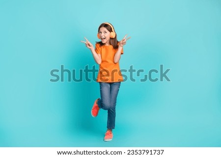 Full length photo of overjoyed positive small girl wear orange stylish clothes hand v-sign epty space ad isolated on cyan color background