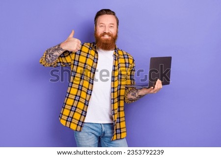 Portrait of cool positive guy hold netbook demonstrate thumb up approval isolated on purple color background