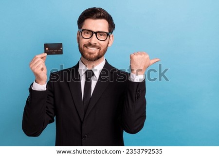 Photo of positive happy banker wear black tuxedo spectacles rising credit card thumb empty space isolated blue color background