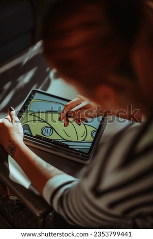 Close up of tattoo artist drawing a yellow car on her tablet  at the table