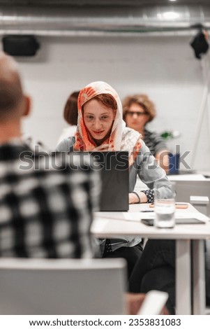 Happy, positive, successful, ginger female business person working on lap top at work gathered at table with her teammates. Front view photo
