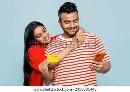 Young couple two friends family Indian man woman wear red casual clothes t-shirts using mobile cell phone credit bank card shopping online book tour together isolated on plain blue color background