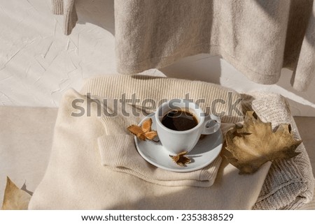 Autumn aesthetic still life with coffee cup, light brown fall leaves, light beige knitted sweaters in sunlight with natural shadow. Neutral pastel lifestyle autumn background. Royalty-Free Stock Photo #2353838529
