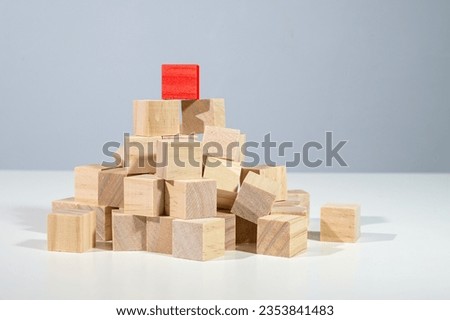 Red cube standing on the top of a heap from light wooden cubes, concept for business, career, and success, gray background with copy space