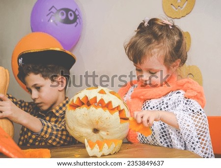 Children wearing Halloween costumes carving holiday pumpkins for home decoration