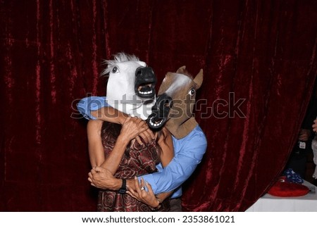 Photo Booth. Unidentifiable People wear Horse Head Masks and pose and play while their pictures are taken in a Photo Booth. Party Photo Booth. Wedding Photo Booth. Holiday. Horsing Around. Fun Times.
