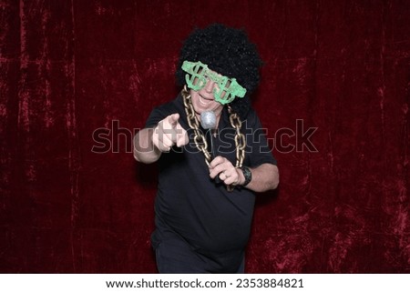 Photo Booth. A man Smiles and Laughs as he poses for his picture to be taken while in a Photo Booth at a Party. People love to pose with Props and their friends in  Photo Booths at Parties. Holidays. 