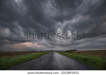 WEATHER - Dramatic black rain clouds over fields and country road Royalty-Free Stock Photo #2353892453