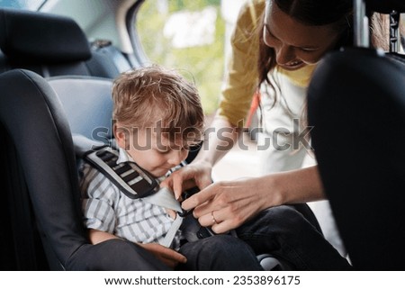 Young mother buckling toddler into child safety car seat. Royalty-Free Stock Photo #2353896175