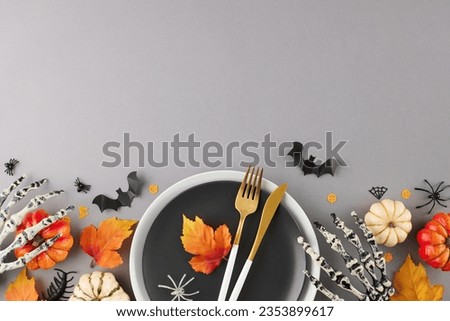 Infusing your table with the spirit of Halloween celebration. Top view of plates, cutlery, pumpkins, scary skeleton hands, autumn leaves, sinister accessories on grey background with ad area