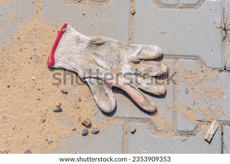Freshly paved sidewalk . Sand and worn protective glove on paving stones.Pavement paving completed. Scattered sand and a discarded old work glove.