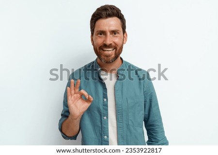 Handsome smiling man standing on white background and showing ok sign with fingers