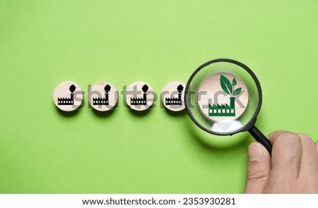 Hand holding magnifier glass and focusing to green factory among pollution manufacturing for green economy to reduce carbon dioxide emission from Kyoto protocol within 2050 ,Sustainability environment