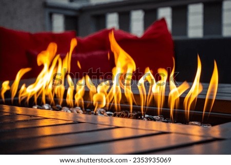 close up of a metal fire table with red cushions in the back gro