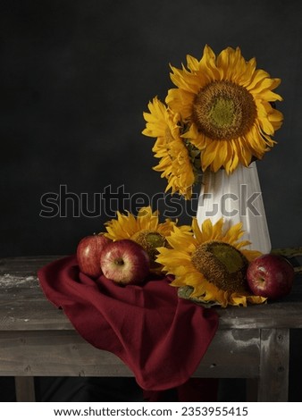 Autumn still life photography with Sunflowers and apples on old wooden table. The table is covered with a red cloth 