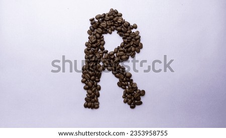 Roasted brown coffee beans arranged in letter R shape and studio lighting on a transitional light blue pink color background.