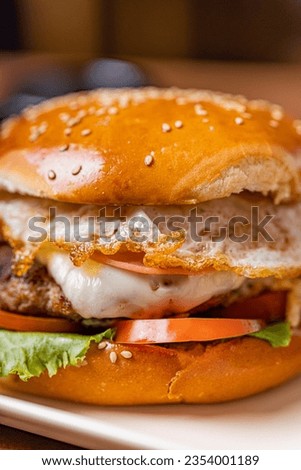 Hamburger with egg and meat, accompanied by french fries, on a plate with creams on a wooden table.