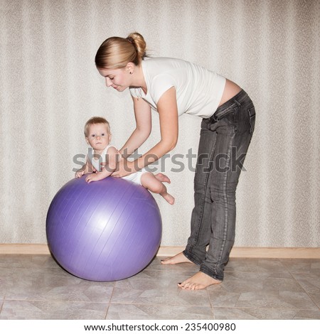 Baby doing exercises at home on fit ball together with mother  