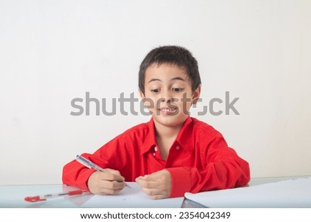 
A cute boy in red shirt sitting and writing doing homework.
The cute boy wearing a red shirt.
emotion through the face.
Studio portrait, concept health with white background.  
funny face.
