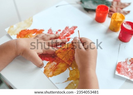 Little girl painting on autumn yellow leaves with gouache, kids arts, children creativity, autumn art. Royalty-Free Stock Photo #2354053481