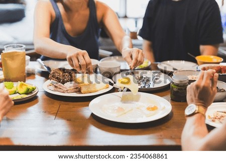 Woman eating fried eggs breakfast with friends on wooden table Royalty-Free Stock Photo #2354068861