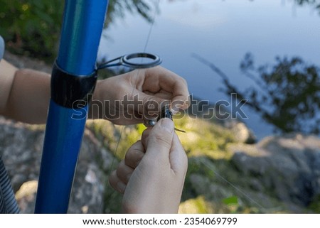 A close-up of the hands of a teenager who takes a small fish off the hook. Sport fishing on the river in summer.