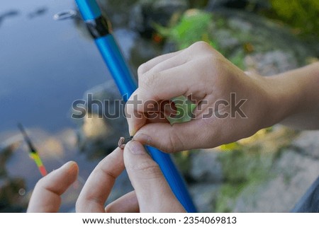 Close-up of a teenager's hands putting bait on a fishing hook Sport fishing on the river in summer.