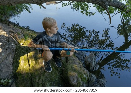 A boy squats on rocks and catches fish. Sport fishing on the river in summer.