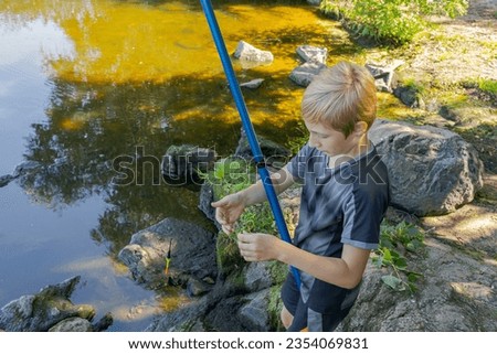 The boy prepares to cast his fishing rod, having prepared a hook and bait. Sport fishing on the river in summer.