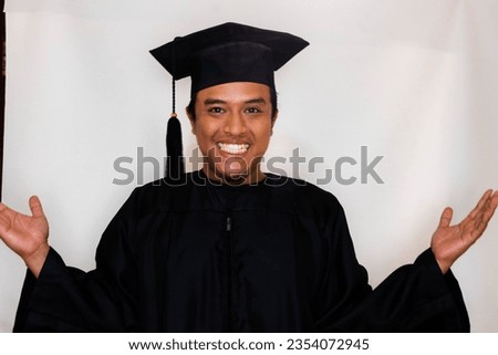 Adult Asian man is smiling excitedly while spreading his hands as if he is welcoming something happily by wearing a toga for graduation. 