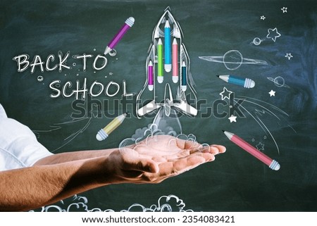 Close up of hands holding abstract back to school sketch with pencils and rocket on chalkboard wall background. Education and knowledge concept