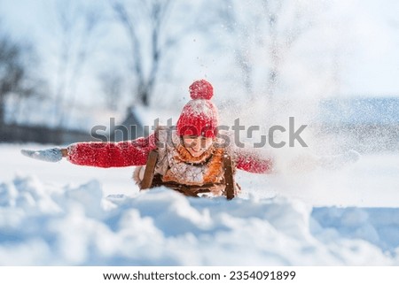 Funny little child runs on sledge in snow. Active sports games in winter time. Happy winter holidays concept.