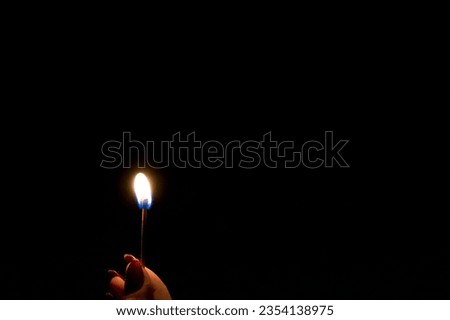 A Matchstick - a photo of a small flame held by a hand with red fingernails.