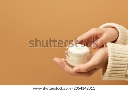 Cropped view of female hands holding container with cream in hands. Using cosmetics product isolated beige background. Concept of body and skin care, spa, dermatology. Copy space for ad