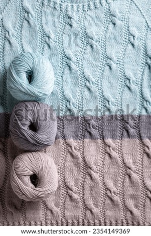 Cotton cashmere balls yarn over abstract turquoise gray knitted pattern background texture with cables. Top view of knitting clothes Royalty-Free Stock Photo #2354149369