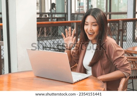 Young Asian woman doing video conference on laptop computer while sitting at the cafe, having meeting