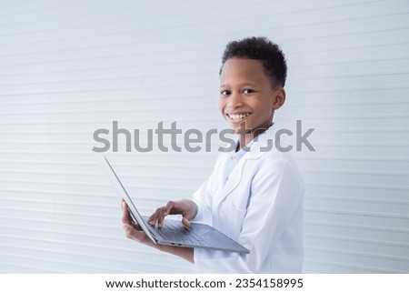 Cheerful African American boy student kid primary school hold modern technology laptop for studying in science class, cute primary school pupils happy looking at camera wearing lab coat uniform