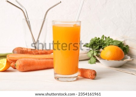 Glass of fresh carrot juice with parsley and orange on white wooden table