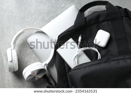 Backpack with powerbank, headphones and laptop on gray background, top view