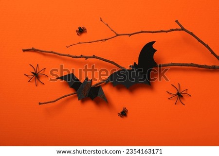 Paper bats and spiders on branch on orange background, top view