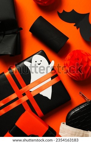 Gift boxes, paper ghost and bat on orange background, top view
