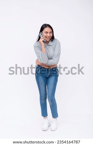 A young asian woman with mid-length talking gingerly to a friend on her cellphone. Possible college student. Isolated on a white backdrop.