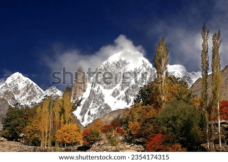 This picture is capture in Hunza Pakistan in this picture snow white Mountains present and green yellow and orange color trees are present. 