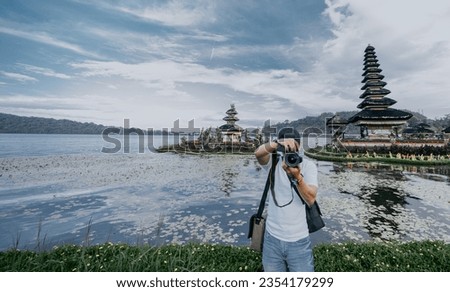 My Real Holiday - Travel photographer taking photos at tourist spots. Indonesian male photographer taking a photo in front of the Bedugul lake temple in Bali.