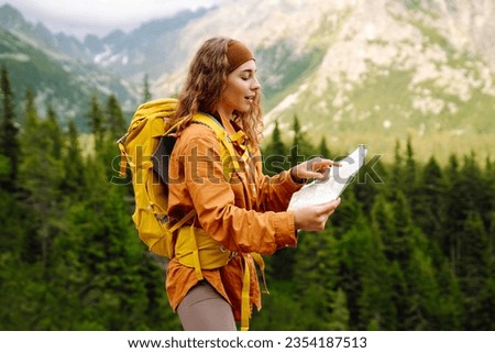 Wanderings. Stylish young woman traveler with a yellow backpack, holds a map, explores hiking trails in the mountains. The concept of travel, vacation.