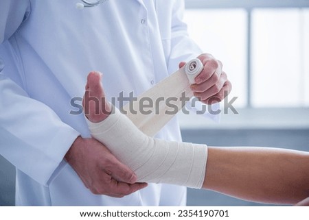 Cropped image of handsome doctor bandaging woman's injured leg while working in his office Royalty-Free Stock Photo #2354190701