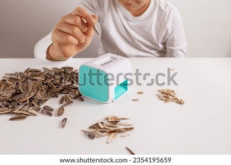 a little kid sitting at a table with sunflower seeds opener, small gadget for open granes, close-up product photo, matching colors