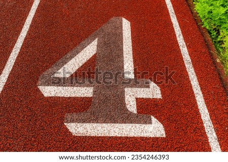 Close up lane number four, 4, on a old red running track with white lane lines, gray numbers, white outline and other markings.	